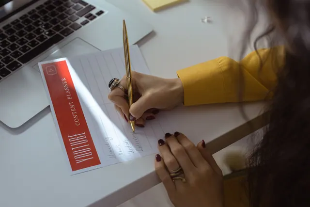 Hand with manicured nails writing in content planner at desk with laptop. Six Content Marketing Strategy Models: From Software to Newsletters