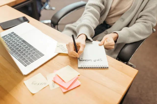 Adult writing notes in a notebook at a desk with a laptop, emphasizing productivity. Are Content Marketing Strategy Teams Still Confusing Traffic With Success?